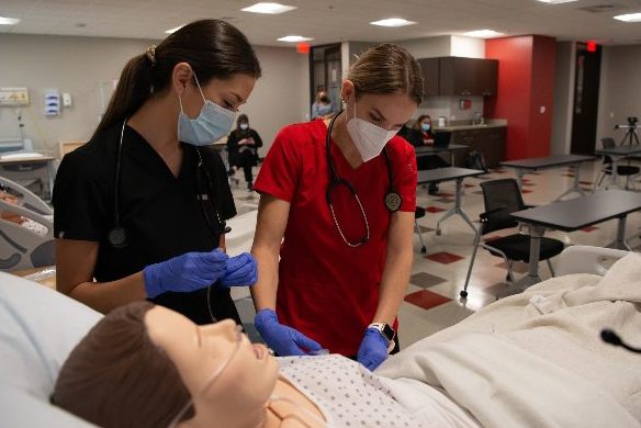 2 UIW ABSN students working together on a practice manikin