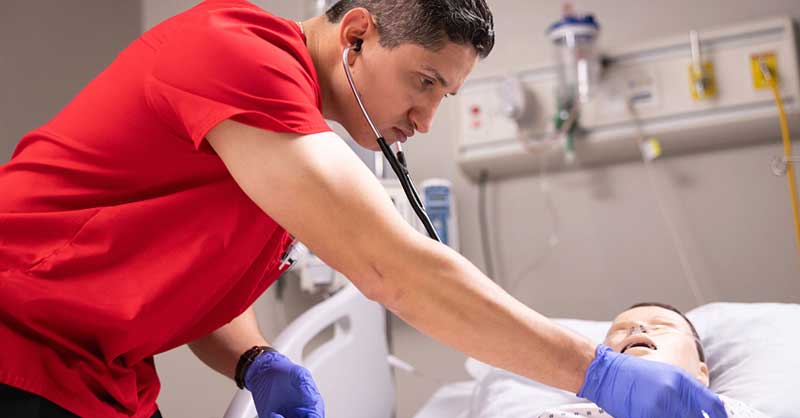 9 Benefits of a BSN in Nursing Nurse in red scrubs working with sim manikin