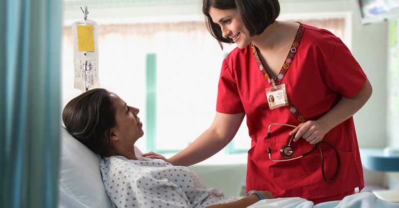 Nurse in red scrubs talking with patient in hospital bed